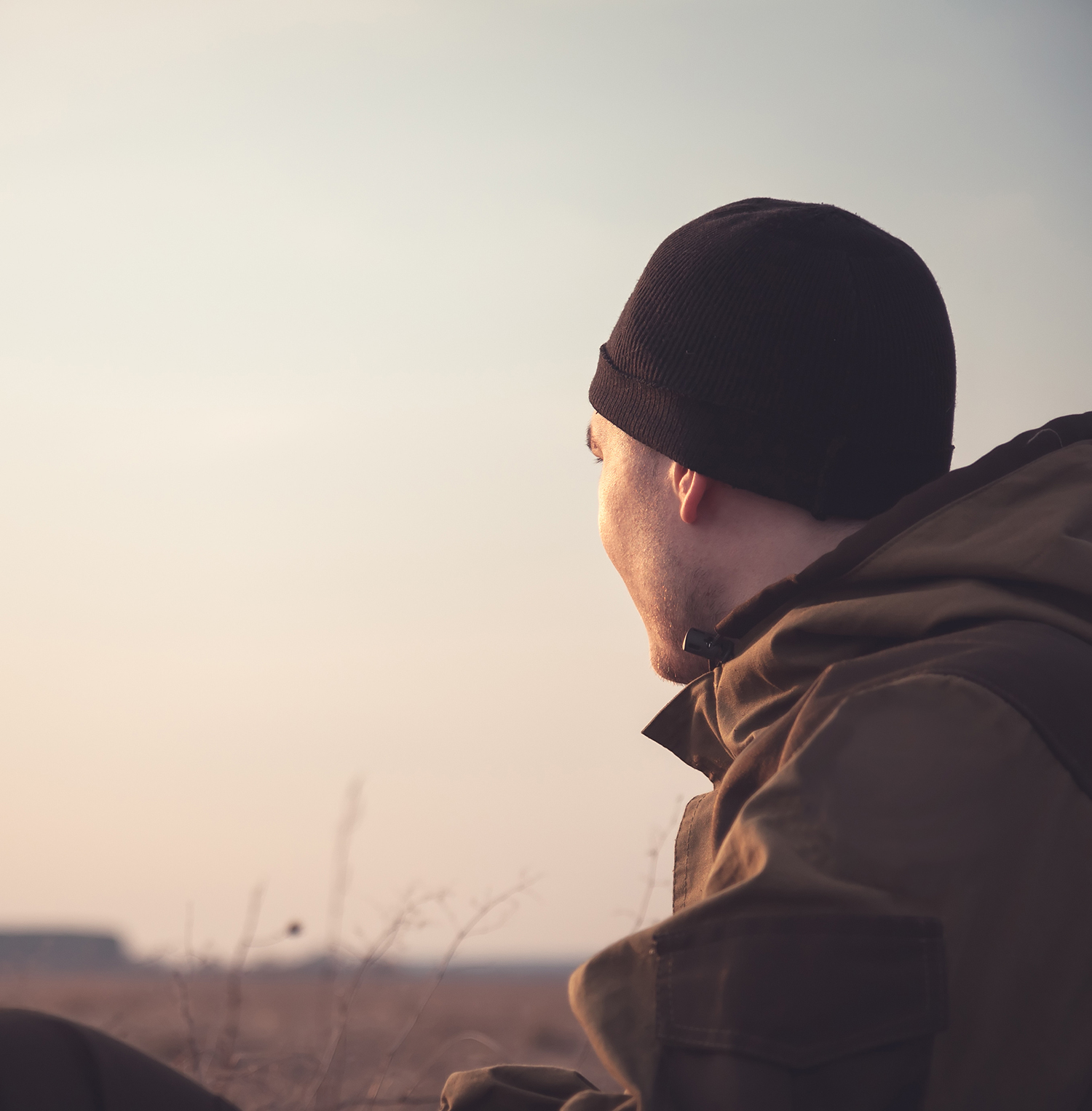 man outdoors in hat and jacket looking into the distance