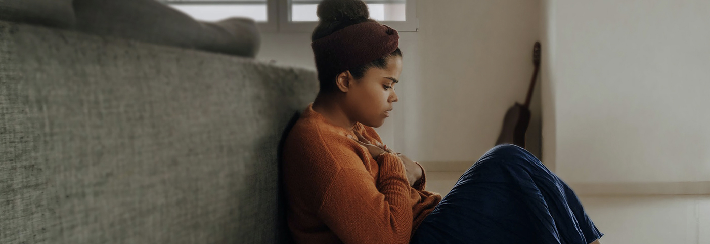 woman sitting on the floor behind a sofa holding her chest