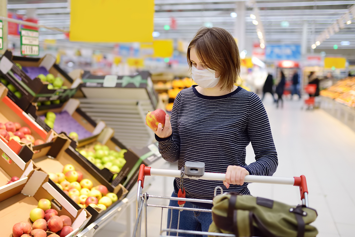 woman shopping at a supermarket with trolley, looking at an apple