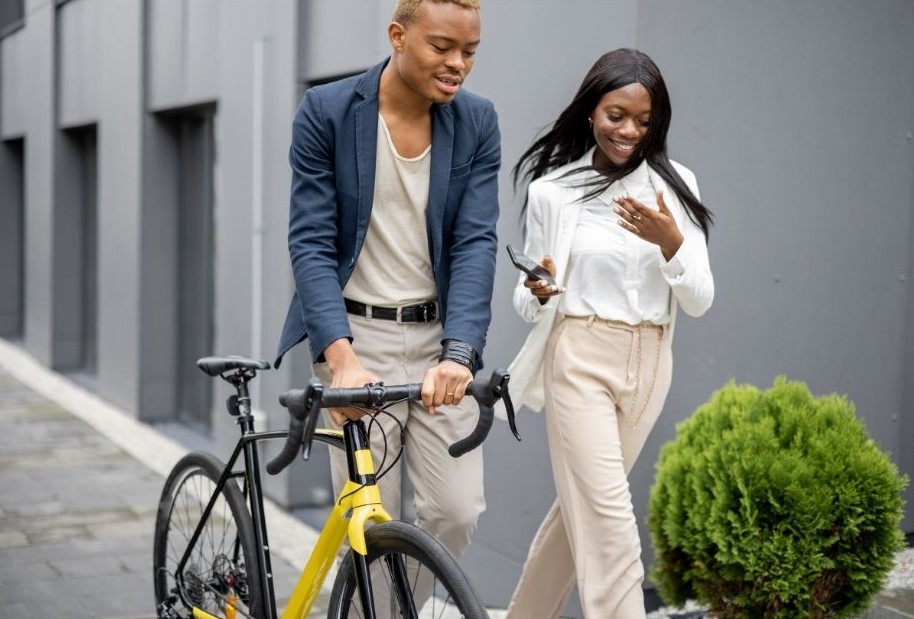 Male and female coworkers walking to work together. The man is pushing a bike along.
