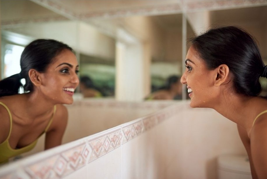 young woman looking into bathroom mirror and smiling