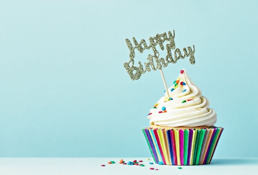 a vanilla cupcake with white icing and sprinkles. The words happy birthday are on a decoration above it