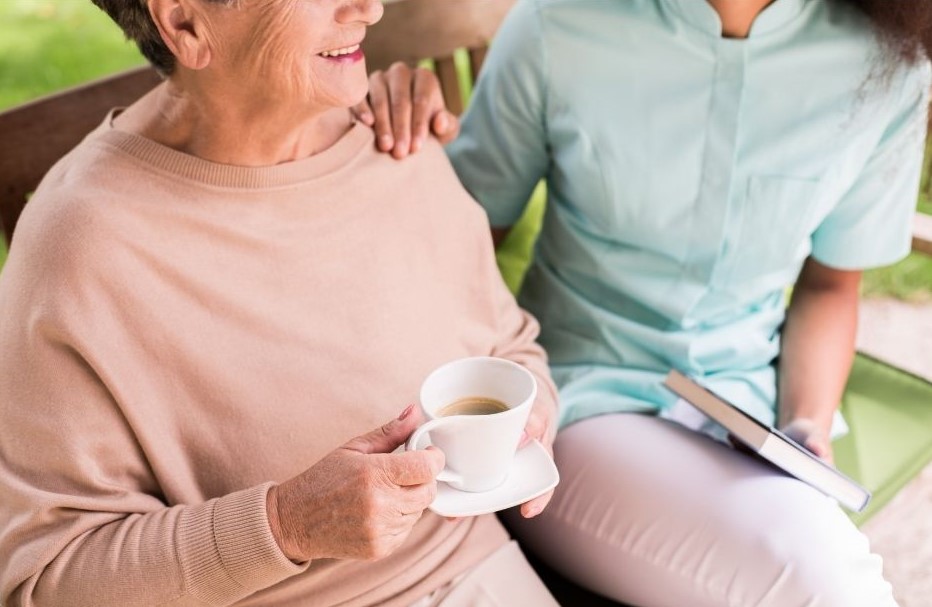 female carer sitting with an elderly lady, who is drinking tea