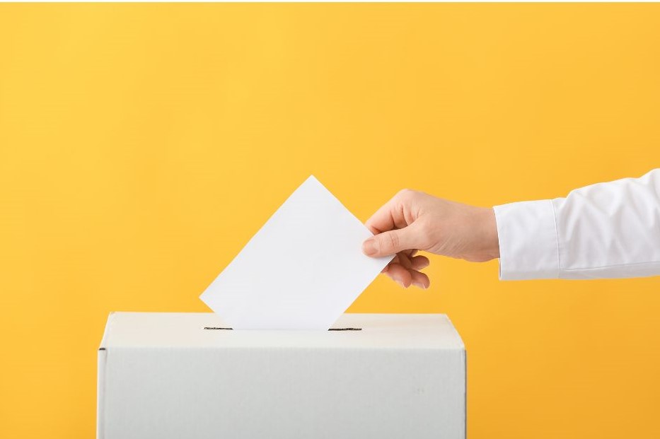 a person placing a voting slip into a ballot box against a yellow background