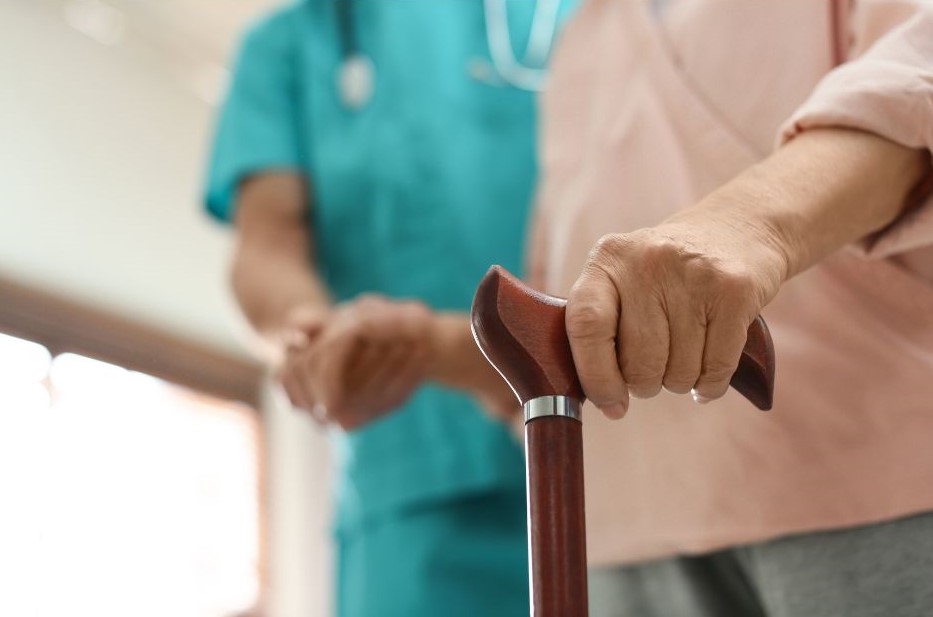 elderly woman with walking stick being supported by care worker