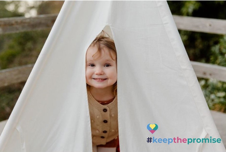 A little girl smiling and sticking her head out of a tent