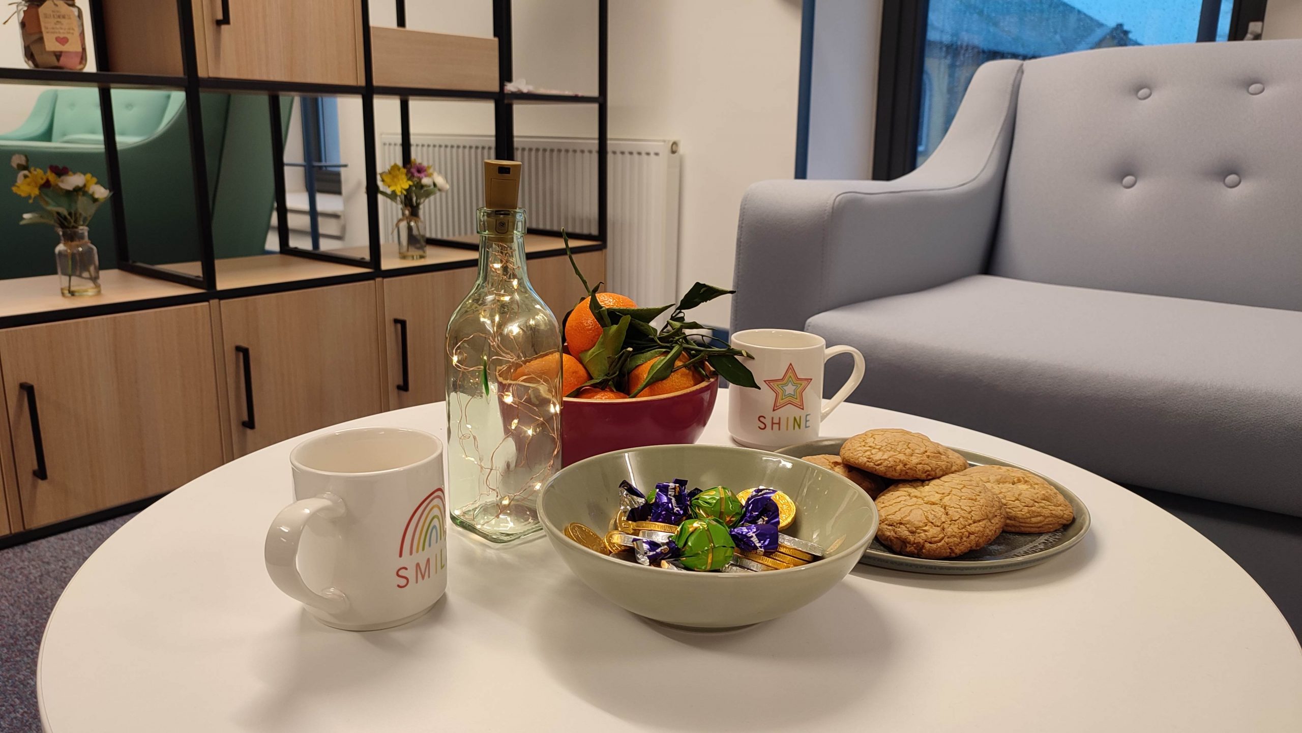 A sofa and coffee table in the wellbeing area, which has a cup of tea and a bowl of sweets