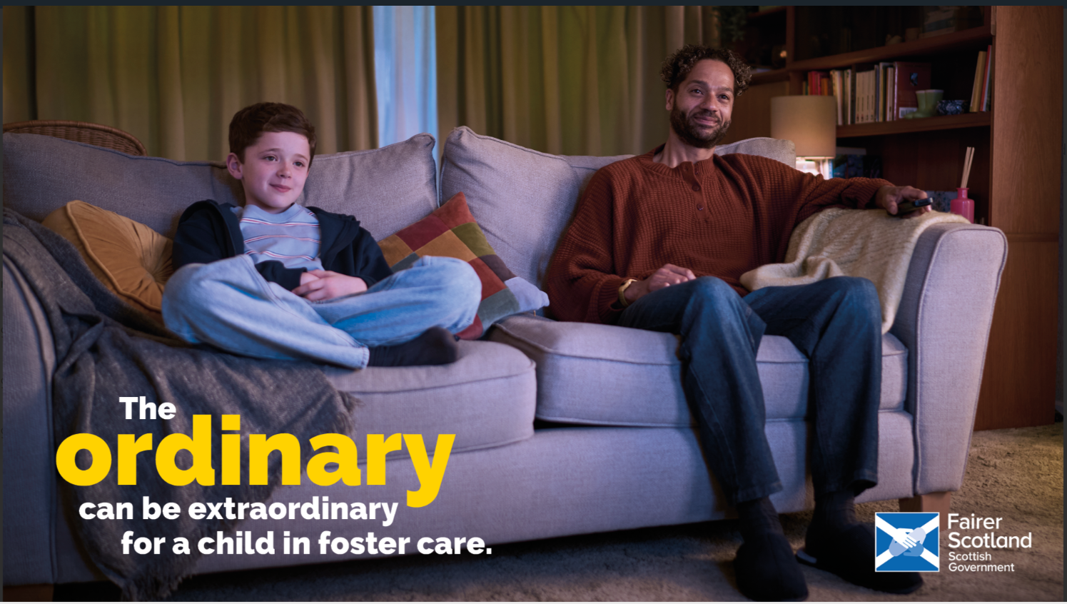 A young boy sitting on a sofa with his foster father as they watch TV together.